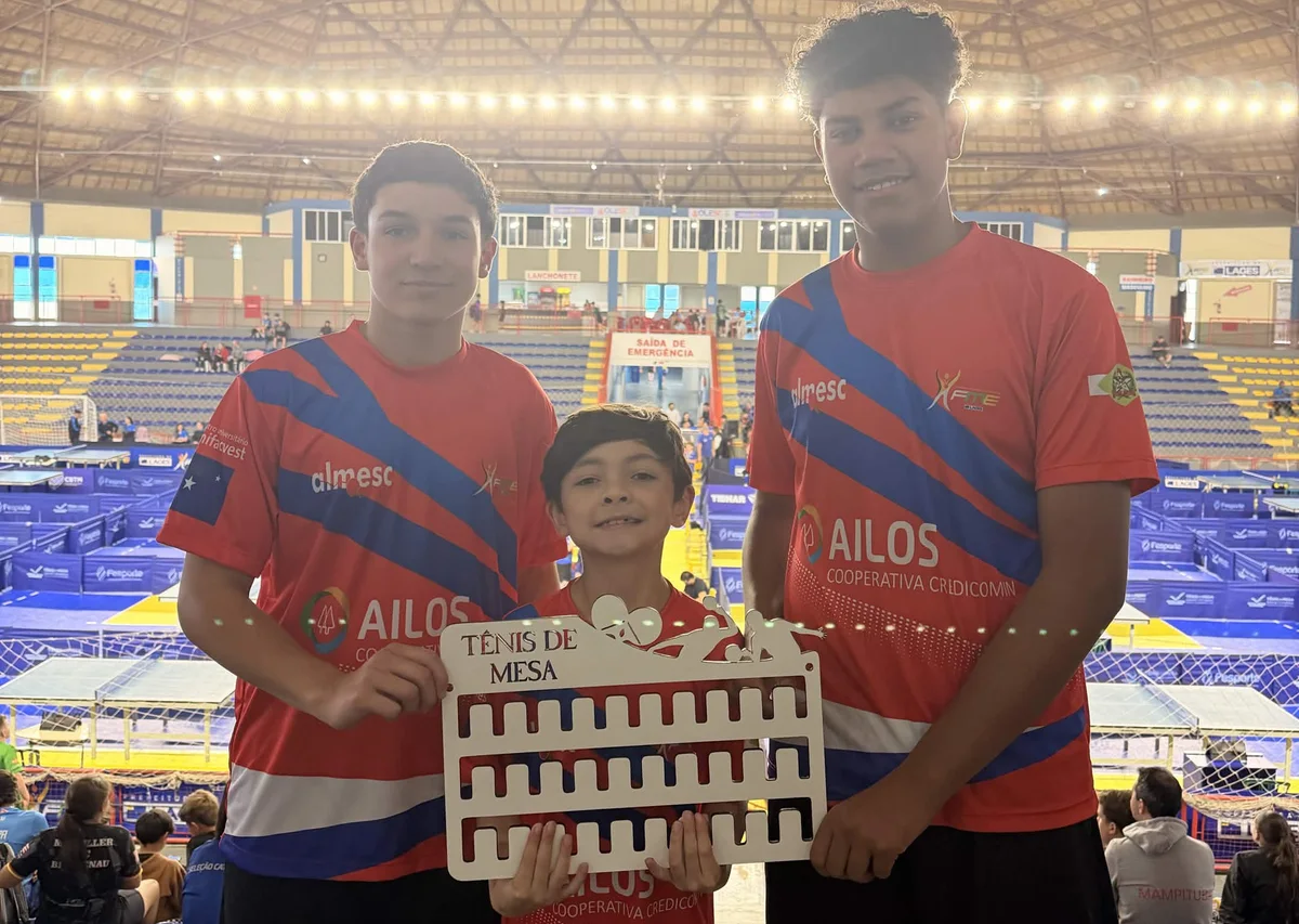 Três atletas da ALMESC, com o uniforme do time, segurando o porta-medalhas no ginásio